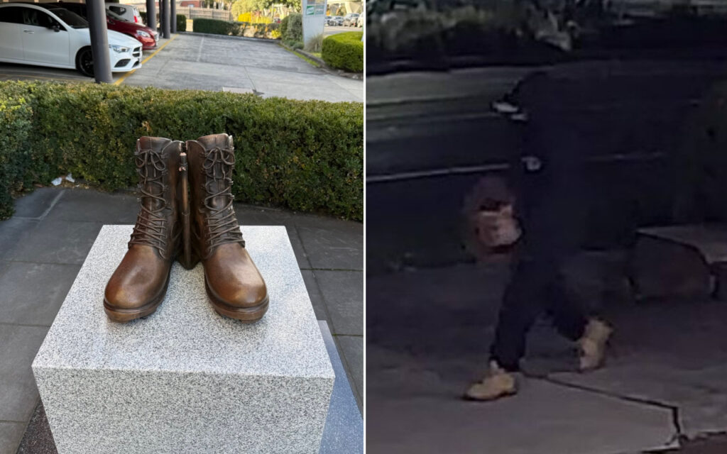 Brown lace-up combat boots displayed upright on a granite pedestal outdoors, with parked cars and greenery in the background.