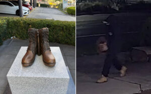 Brown lace-up combat boots displayed upright on a granite pedestal outdoors, with parked cars and greenery in the background.