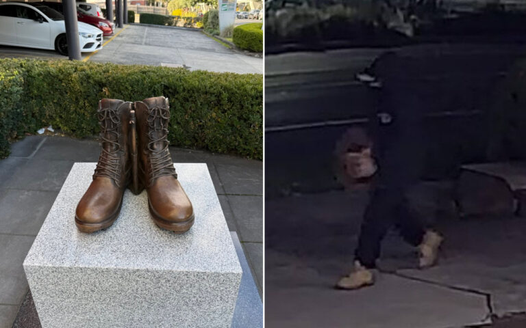Brown lace-up combat boots displayed upright on a granite pedestal outdoors, with parked cars and greenery in the background.