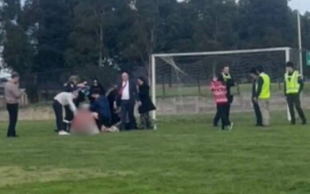 Group of people on a soccer field surrounding a person on the ground near the goal.