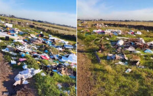 Litter spread across a grassy field along a dirt path: plastic bags, clothes, and discarded items left scattered.