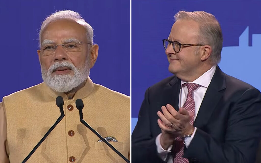 Split-screen of Indian PM Narendra Modi speaking at a beige kurta podium on the left, two microphones in front; a suited man with glasses applauds on the right.