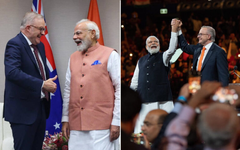 Two men in formal attire shake hands and smile during a ceremony, with flags behind them in the background.