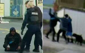 Police officer confronts a man sitting on the curb outside a store as another officer watches nearby.