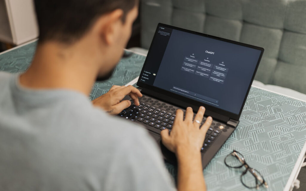 Person typing on a laptop displaying a ChatGPT interface on a patterned table.
