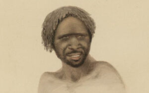 Portrait of a shirtless man with dreadlocks and a short beard, smiling with squinting eyes.