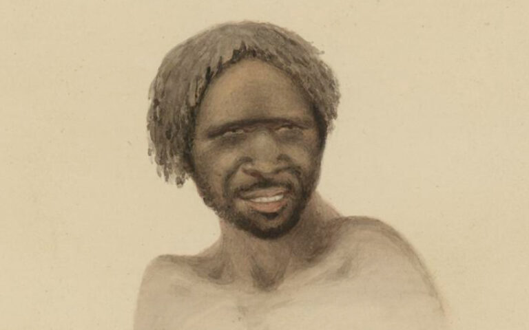 Portrait of a shirtless man with dreadlocks and a short beard, smiling with squinting eyes.