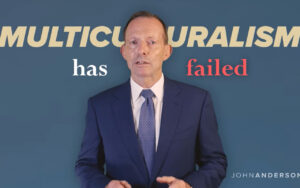 Presenter in a navy suit speaks in front of a blue backdrop with the bold text 'MULTICULTURALISM has failed'.