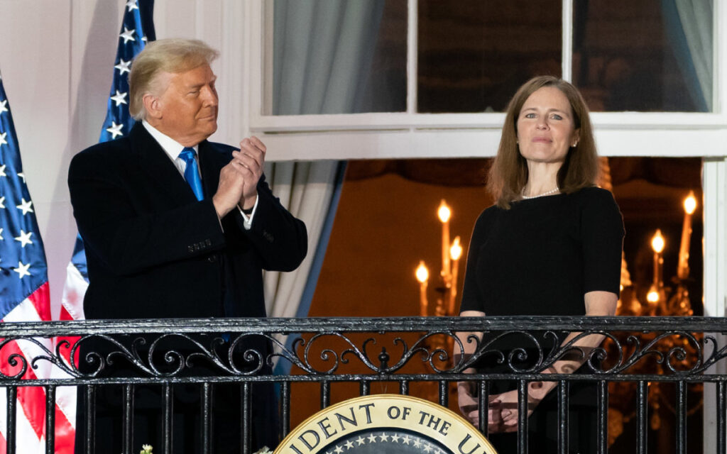 Two adults stand on a balcony with U.S. flags behind them; the presidential seal is visible on the railing.