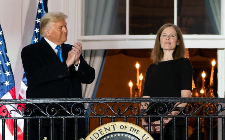 Two adults stand on a balcony with U.S. flags behind them; the presidential seal is visible on the railing.