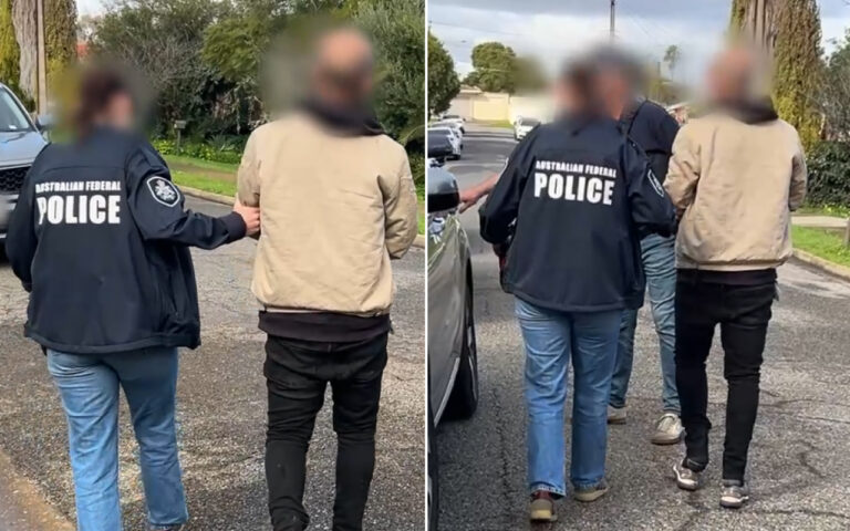 Two Australian Federal Police officers walk a shirtless- or-jacketed man down a suburban street, backs to camera, with blurred faces for privacy.