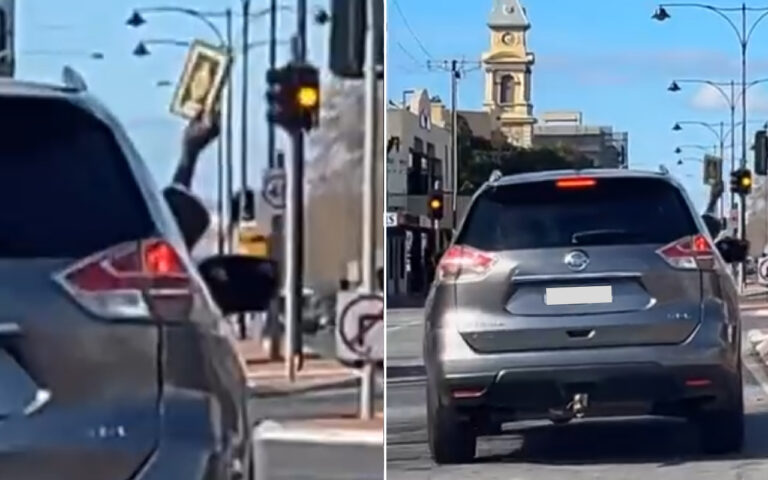 Person in a car at a city intersection raises a framed portrait through the window next to a traffic light.