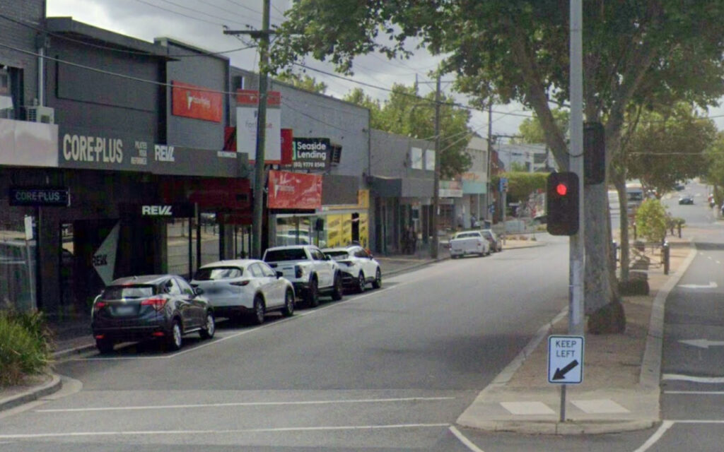 Urban street with storefronts and parked cars along the curb; visible signs read COREPLUS and Seaside Lending; red traffic light ahead.