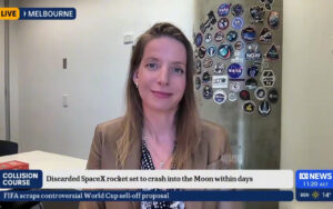 Live Melbourne news broadcast: female anchor in a tan blazer speaks from a studio, with a wall of space patches behind her; lower ticker references SpaceX and the Moon.