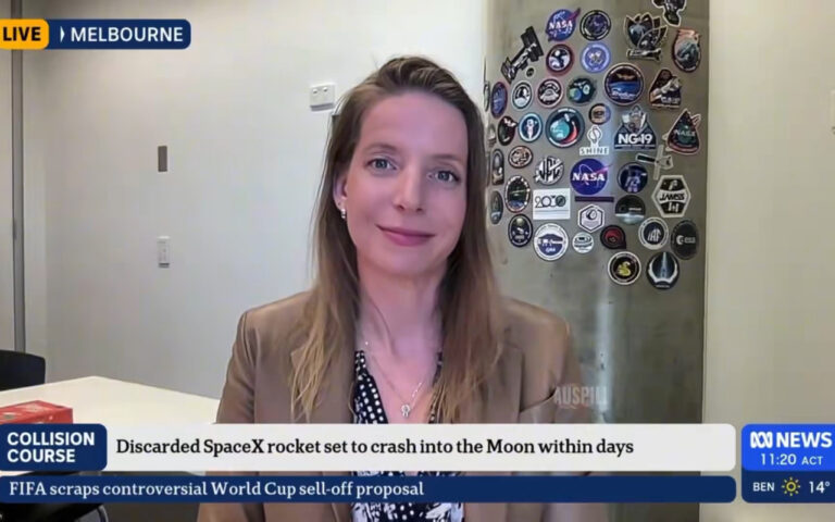 Live Melbourne news broadcast: female anchor in a tan blazer speaks from a studio, with a wall of space patches behind her; lower ticker references SpaceX and the Moon.