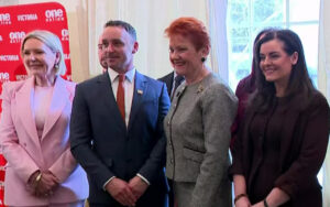 Four people posing for a photo at a formal event, with a red campaign banner in the background.